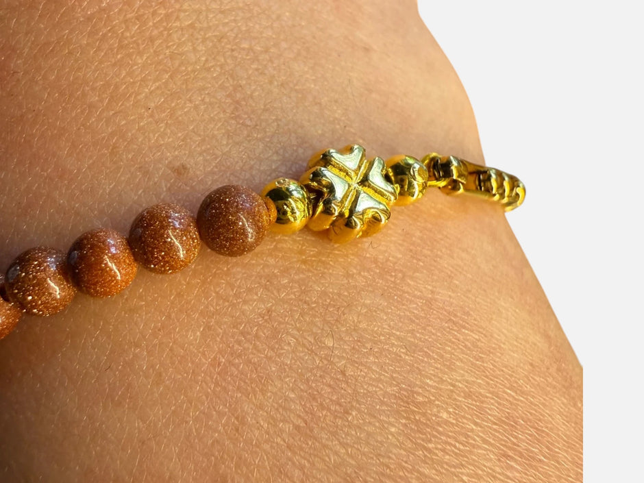 SPARQ armband met bruine zandsteen kralen, goudkleurige schakels en een klavertjevier bedel om een pols
