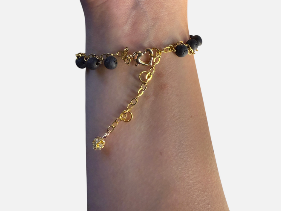 SPARQ Golden Heart Lava Bracelet met zwarte lavastenen, goudkleurige ketting en hartvormige sluiting om een pols.