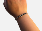SPARQ handgemaakte kralenarmband met grijze en zwarte natuurstenen om een pols bij een raam