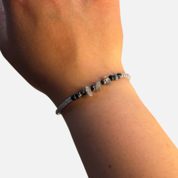 SPARQ handgemaakte kralenarmband met grijze en zwarte natuurstenen om een pols bij een raam