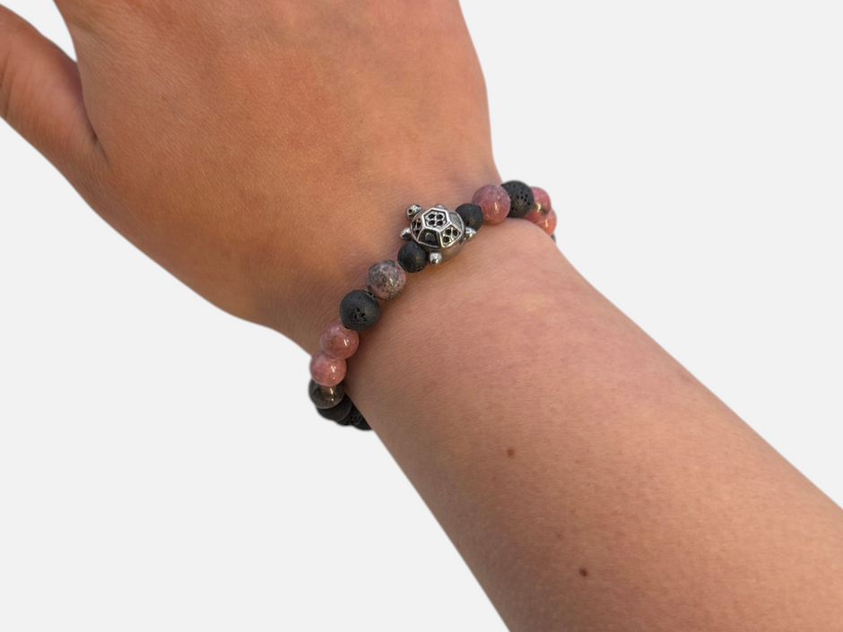 SPARQ kralenarmband met zwarte lavastenen, roze rhodoniet en een zilverkleurige schildpadbedel om een pols.
