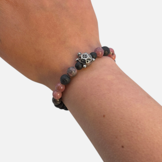 SPARQ kralenarmband met zwarte lavastenen, roze rhodoniet en een zilverkleurige schildpadbedel om een pols.