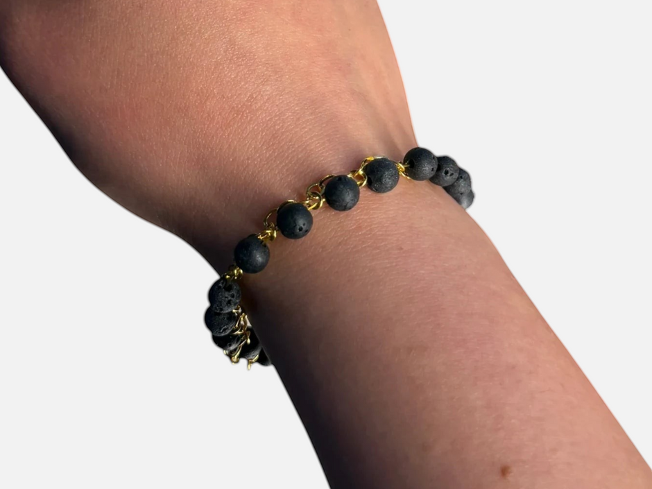 SPARQ armband met zwarte lavastenen en goudkleurige schakelketting om een pols bij daglicht