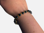 SPARQ armband met zwarte lavastenen en goudkleurige schakelketting om een pols bij daglicht