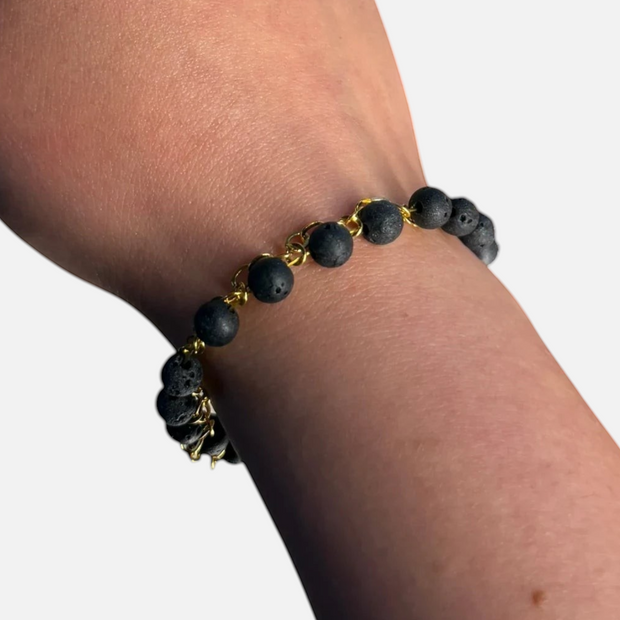 SPARQ armband met zwarte lavastenen en goudkleurige schakelketting om een pols bij daglicht
