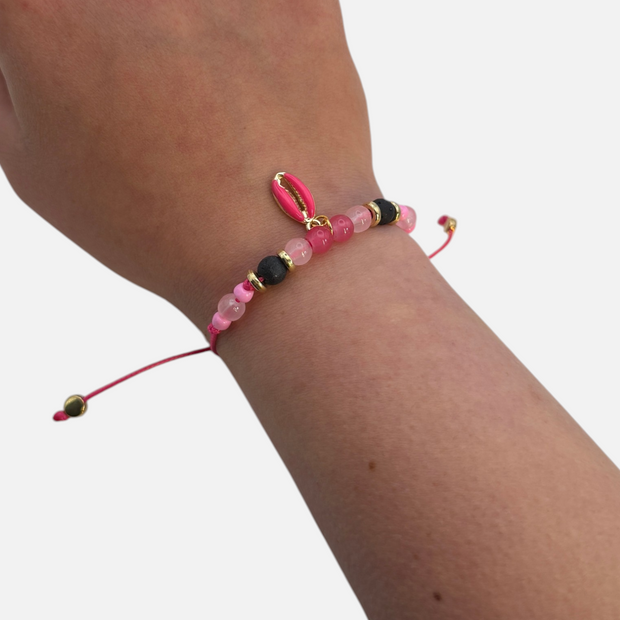 SPARQ handgemaakte roze schelp armband met zwarte kralen en goudkleurige accenten om een pols.