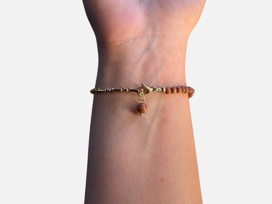 SPARQ armband met bruine zandsteen kralen, goudkleurige schakelketting en een klavertjevier bedel om een pols.