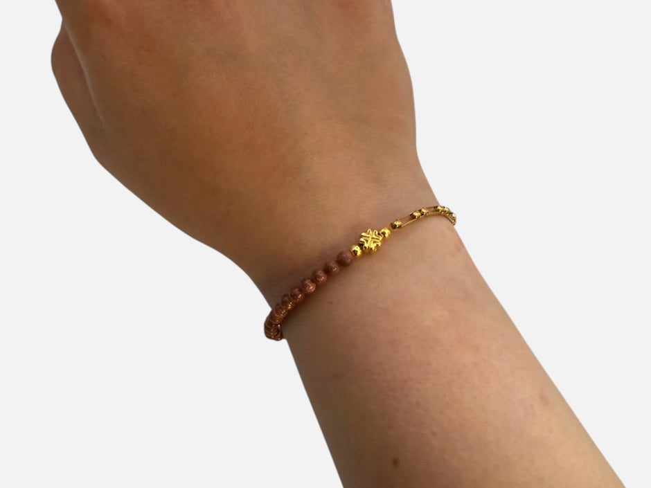 SPARQ armband met bruine zandsteen kralen, goudkleurige schakelketting en een klavertjevier bedel om een pols.