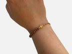 SPARQ armband met bruine zandsteen kralen, goudkleurige schakelketting en een klavertjevier bedel om een pols.
